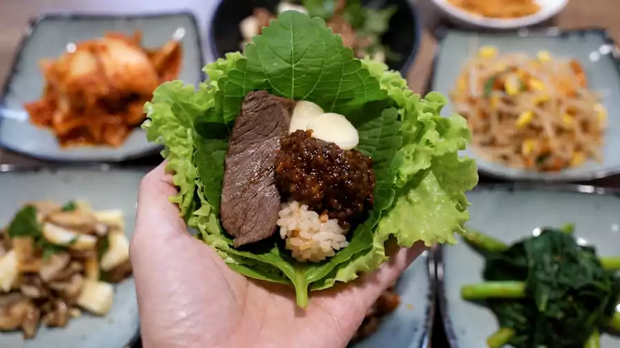 What Is Bulgogi? A Complete Guide to Korean BBQ Favorite | 불고기 3 A hand holding a lettuce wrap (ssam) with grilled bulgogi